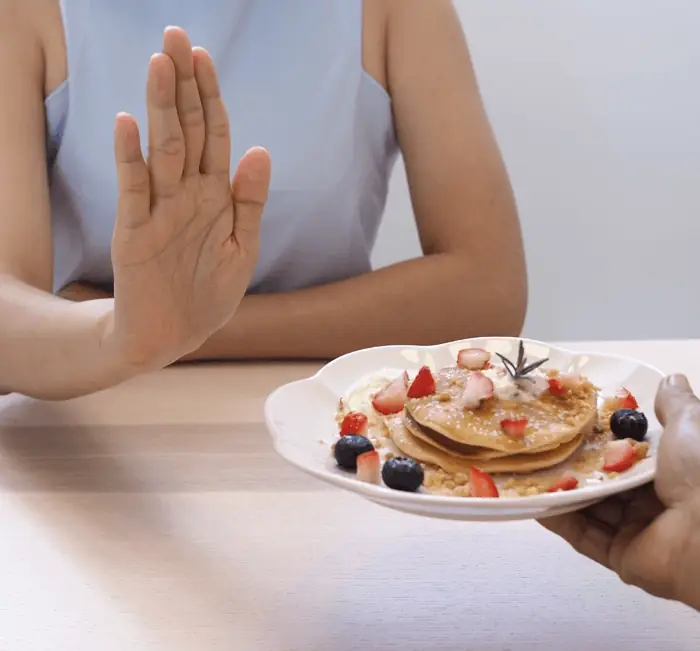 A hand declining a plate of pancakes, illustrating appetite regulation